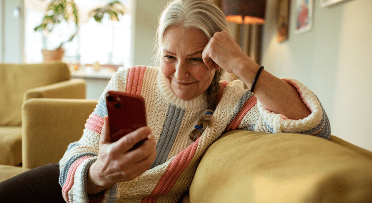 Older woman sitting on the couch smiling and looking at her phone