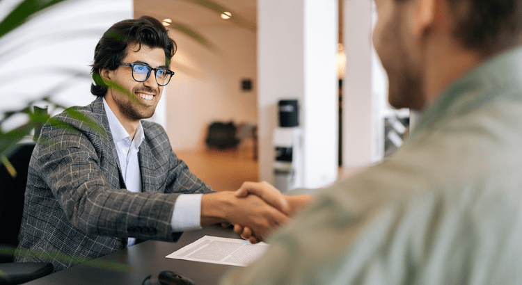 Two gentlemen sitting at a table, shaking hands.