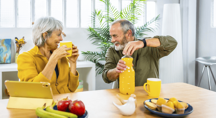 Husband and wife laughing at the breakfast table, enjoying a glass of orange juice.